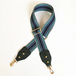 Detail of adjustable wide woven bag strap with navy and teal geometric embroidery and gold hooks