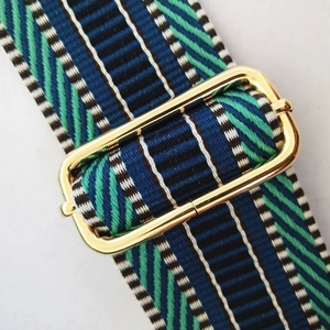 Macro shot of thick embroidered bag strap with navy and mint geometric stripes and gold buckle