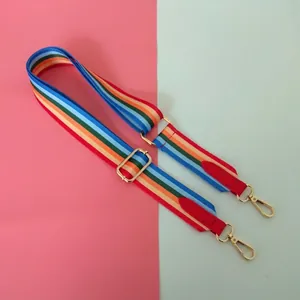 Close-up of a wide rainbow striped woven bag strap with golden buckles and red leather ends