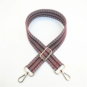 Close-up of ethnic geometric wave pattern on red and white woven bag strap with gold buckle