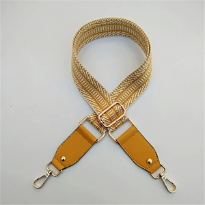 Detail of yellow and white woven purse strap with golden metal swivel hooks and buckles