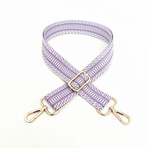 Detail of a wide woven purse strap with purple and white geometric patterns and gold clips