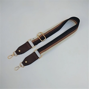 Close-up of adjustable striped canvas bag strap with leather ends and gold metal hooks