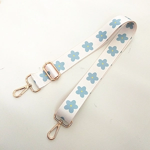 Détail d'une bandoulière de sac réglable avec motif floral bleu et mousquetons dorés