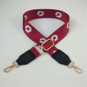 Detail of burgundy wide strap with daisy pattern and golden metal swivel hooks