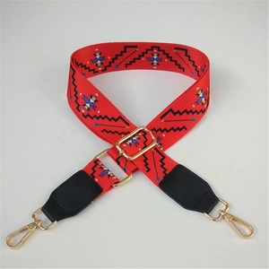 Detail of red geometric tribal pattern wide strap with gold metal hooks and leather ends