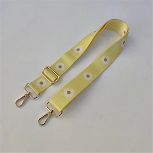 Close-up of yellow daisy pattern wide strap with gold rotating swivel hooks and slider