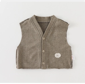 Detail of brown knit baby vest featuring a V-neck, three buttons, and a monday patch