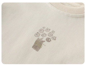 Close-up of ribbed crewneck and cat print on cream-colored soft cotton baby sweatshirt
