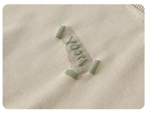 Detailed close-up of beige knitted fabric with green 3D towel embroidery and YOOTA text