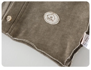 Detail of baby cotton jacket featuring textured brown button and house pattern embroidery