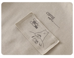 Detailed close-up of beige cotton fabric with minimalist bear illustration and fine stitching