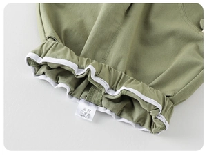 Close-up of elastic waistband on green cotton baby pants with white piping and care label