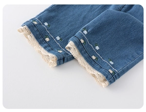 Dettaglio di jeans da bambina con ricami floreali e bordo in pizzo bianco rifinito
