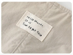 Macro detail of beige fabric with 'Hello Winter' text patch on toddler overalls