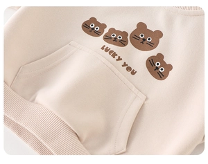 Close-up of baby beige sweatshirt with cartoon bear print and front pocket detail