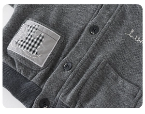 Detail view of dark grey knit jacket showing bird patch and artistic embroidery