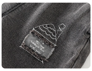 Detailed close-up of dark grey denim embroidery featuring a house patch and artistic text