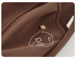 Close-up of brown cotton kids trousers featuring a white house print and wooden button detail