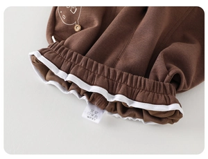Detail view of brown knit baby pants with ruffled waist and white side graphic print
