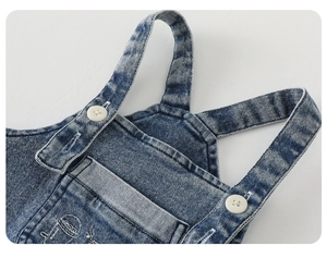Détail de la salopette en jean bleu montrant la poche poitrine avec broderie blanche et boutons
