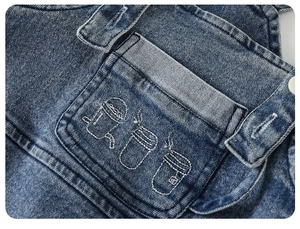 Gros plan d'une salopette en jean pour enfant montrant broderie et détails de couture