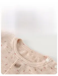 Détail du cardigan rose côtelé pour bébé avec imprimé fleuri, boutons et fleur tricotée