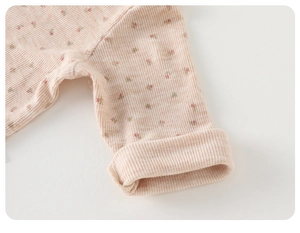 Détail des poignets en maille côtelée à fleurs roses sur gilet bébé en coton doux rose