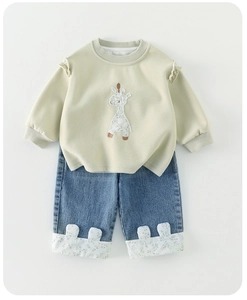 Detail of ruffled shoulders and giraffe embroidery on cream sweatshirt and floral jeans