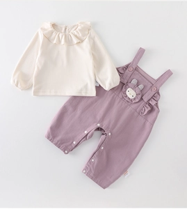Detail of baby girl outfit with lilac overalls, rabbit embroidery and ruffled cream top