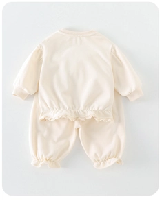 Détail de sweat pour bébé crème avec ourlet en dentelle et poignets à volants doux