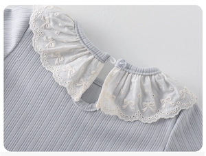 Detail showing layered white lace collar with embroidered bow patterns on girls knit top