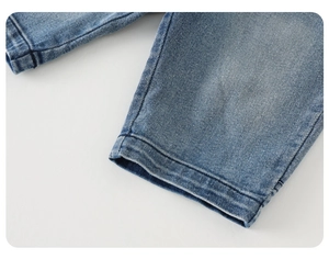 Detailed macro shot of light blue washed denim pants showing hem stitching and fabric texture