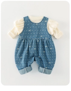 Detail of baby girl outfit with white ruffled top and blue polka dot bow overalls