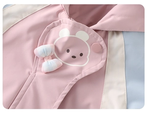 Detalle de chaqueta rosa con estampado de oso, botones de presión y un lazo