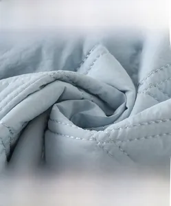 Macro shot of light blue quilted fabric showing soft diamond stitching for baby clothing