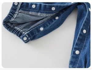 Detailaufnahme der Baby-Jeanslatzhose mit runden Druckknöpfen und elastischen Bündchen
