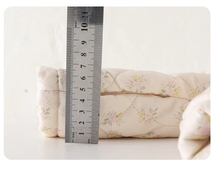 Detailed macro view showing the thickness of the floral quilted fabric with measuring tape