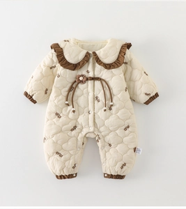 Détail d'une grenouillère matelassée pour bébé avec imprimé floral et col à volants brodé