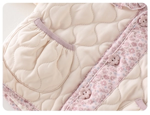 Détail d'un gilet matelassé pour fille avec passepoil fleuri et boutons fleurs
