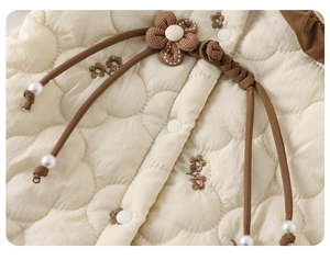 Détail d'une barboteuse bébé matelassée blanc cassé avec broderie florale et perles