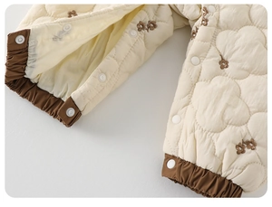 Détail d'une barboteuse matelassée pour bébé avec broderie florale et boutons-pression