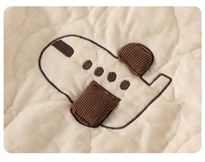 Detail of baby quilted jacket featuring cartoon airplane patch with brown corduroy texture
