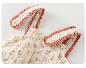 Close-up of quilted floral baby romper showing pink corduroy ruffles and button detail
