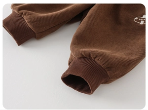 Close-up of coffee brown corduroy pants with elastic ribbed cuffs and white airplane embroidery