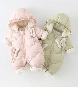 Detail of baby winter romper showing ruffled hood and delicate 3D bow on quilted fabric