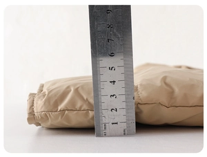 Close-up showing the 5cm thickness of a khaki quilted down vest with a metal ruler