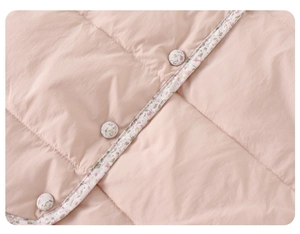 Détail du gilet en duvet matelassé rose avec boutons floraux et bordure assortie