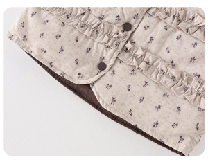 Macro shot of floral pattern on kids down vest with ruffled trim and brown buttons