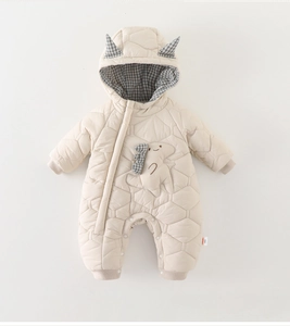 Détail de la barboteuse beige matelassée avec texture hexagonale et écusson dinosaure